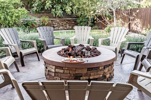 A raised fire pit surrounded by chairs in a back yard.